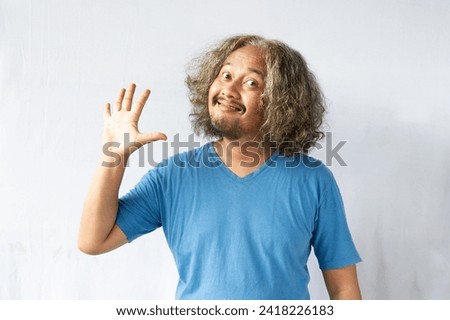 A handsome, curly-headed man wearing light blue clothes stood and laughed with his hands raised showing numbers. Photo of cheerful man isolated on white background.