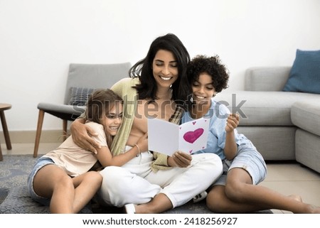 Happy Latin mom hugging adorable son and daughter with love, gratitude, holding greeting card with drawn heart, smiling, laughing, celebrating birthday, mothers day