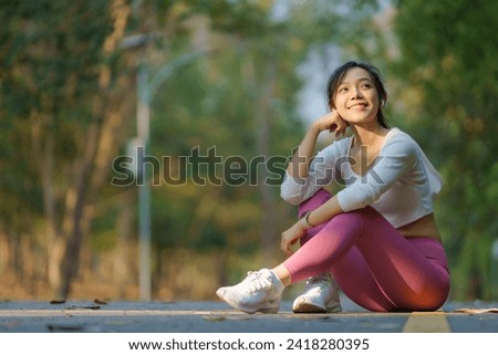 An Asian woman sits on the sidewalk, enjoying a well-deserved rest after a run in the park.