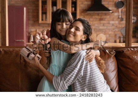 Happy holiday, dear mommy. Affectionate single latina mother hug tight beloved child preteen girl receive surprise in gift box and flowers on Mothers Day. Loving little kid congratulate mom on March 8 Royalty-Free Stock Photo #2418283243