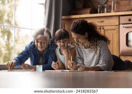 Family leisure. Friendly happy dynasty 3 latin females of different ages preteen girl kid older grandma young mom relax at home kitchen lying on warm floor drawing painting pictures with watercolors
