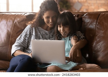Parental control. Smiling latina mommy and preteen junior school age daughter child chat in computer app make purchases at web shop online. Happy young nanny and little girl friends use laptop at home