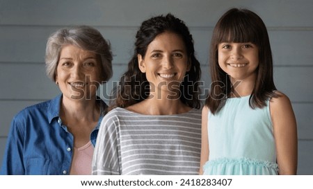 Mothers and daughters. Happy intergenerational latin family of 3 diverse age females pose for portrait together. Cute little girl look at camera smile standing with millennial mom and old age grandma