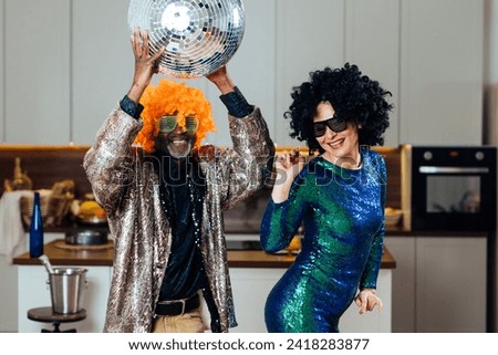 Cinematic image of an happy multiethnic senior couple making party. Indoors Lifestyle moments at home. Concept about seniority and relationships