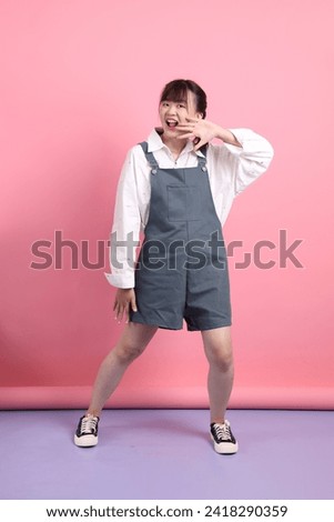 Cheerful lovely young asian woman in overalls casual clothes with gesture of posing isolated on pink background. St Valentine's Day, Women's Day, Birthday