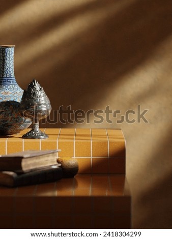 Versatile product placement: Orange-tiled tiers host a curated scene. A vase, incense burner on top; two stacked books below. Play of light and shadow. Lifestyle blending warmth and creativity. Royalty-Free Stock Photo #2418304299