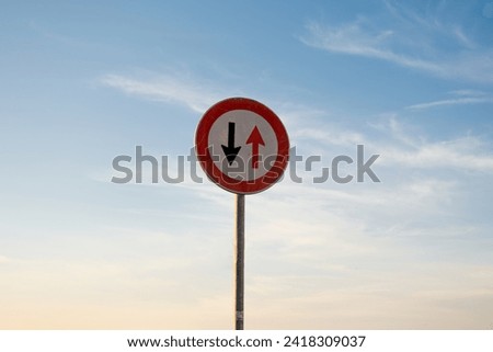 Give way to oncoming vehicles traffic sign, isolated sunset sky.