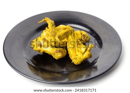 Indonesian yellow spice fried chicken wings on a black plate on an isolated background. savory food