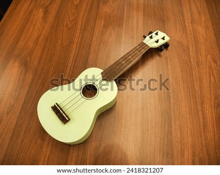 A pastel green ukulele with a wooden fretboard rests on a wooden floor, its strings inviting a musical touch. Royalty-Free Stock Photo #2418321207