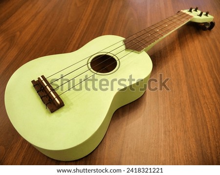 A pastel green ukulele with a wooden fretboard rests on a wooden floor, its strings inviting a musical touch. Royalty-Free Stock Photo #2418321221