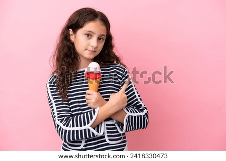 Little caucasian girl holding an ice cream isolated on pink background pointing to the side to present a product