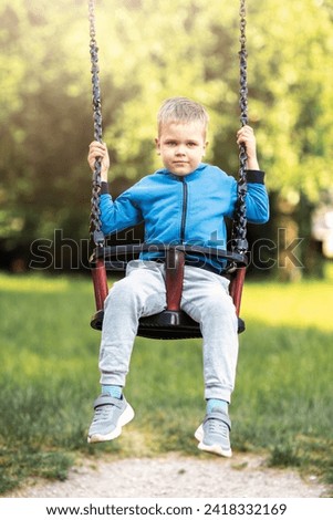 Dreaming preteen schoolboy plays swings under high tree at sunset light. Smiling little boy swings and resting on summer holiday.