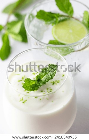 A refreshing and healthy summer composition featuring a yogurt cup, lime, and mint against a backdrop of green and white, capturing the essence of a light and nutritious diet. Royalty-Free Stock Photo #2418340955