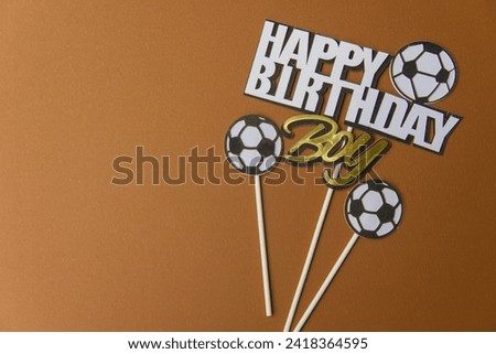 The poster wishes a happy birthday to a boy on a horizontal brown background with text and a soccer ball symbol. Place the main object in free space on the left-hand side of the image.