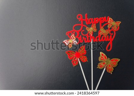 Letters with paper butterflies wishing Happy Birthday on a black background with red letters and space for white light hitting the background adding dimension to the image suitable for postcards signs
