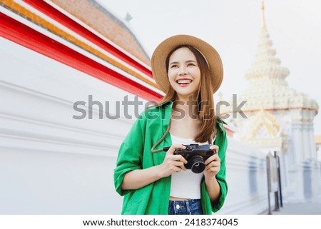 Young Asian woman traveler wearing green shirt with taking picture using a camera at temple. summer tourism concept.