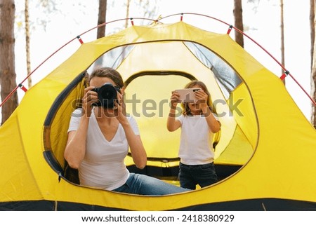 A girl with a child taking pictures of nature while in a tourist tent. A family on vacation in a yellow tourist tent away from the bustle of the city. The time spent by the family together in nature