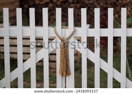 A beige rope knot hangs on a white wooden picket fence, evoking simplicity and rustic charm. Concept for home decor, DIY crafting inspiration or site page login, sign in.