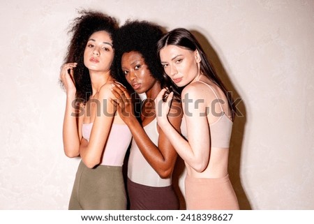 Three beautiful alluring mixed race girls standing near the wall, African and White Caucasian young women. Female fashion models wearing leggings and tops.