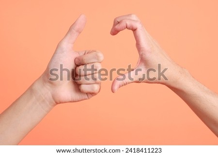 The two hand of Asian man connected each other with heart sign and thumb up sign on the pink background.
