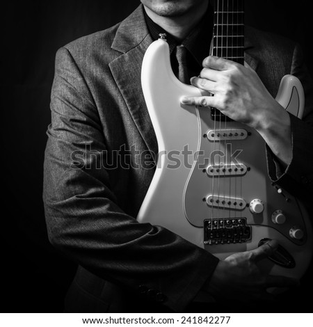 male musician in grey suit holding electric guitar on dark background