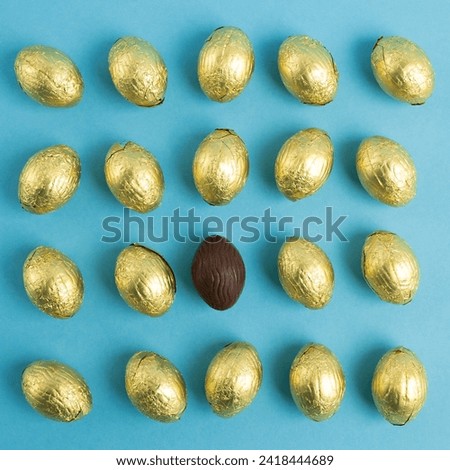 Top view of chaotically decomposed golden wrapped Chocolate Easter eggs and unique one on blue background, diversity and inclusion