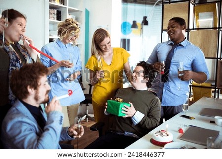 Businessman holding gift celebrating birthday with colleagues in office