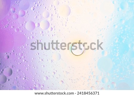 Abstract background in lilac and blue soft tones. Macro drops of oil on the surface of the water. Delicate cosmetic background for advertising products. Copy space  Royalty-Free Stock Photo #2418456371