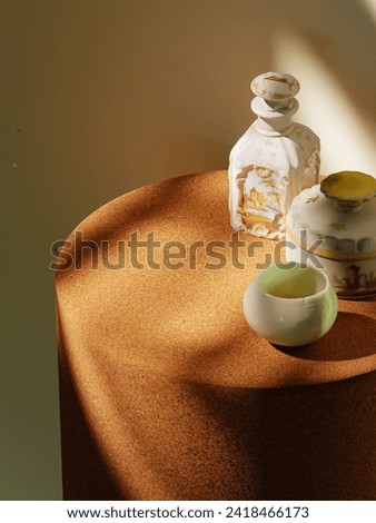 Vintage allure: Cork side table with intricate bottle, jar, and ceramic cup. Abstract shadows and light dance. Ideal for creative product placement, merging vintage charm with modern sophistication. Royalty-Free Stock Photo #2418466173
