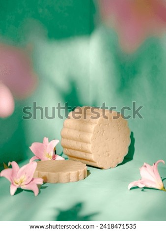 Handmade serenity: Artisanal soap-like cylinders on light green backdrop with pink flowers. Perfect for creative product placement, blending natural charm into your brand narrative. Royalty-Free Stock Photo #2418471535