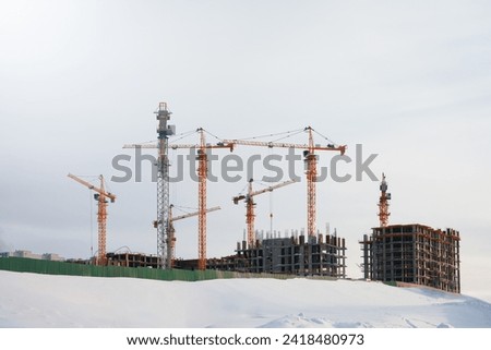 Construction of a new neighborhood. Winter. Panoramic view of a snow-covered construction site with many construction cranes against the cold sky. Copy space.                                Royalty-Free Stock Photo #2418480973