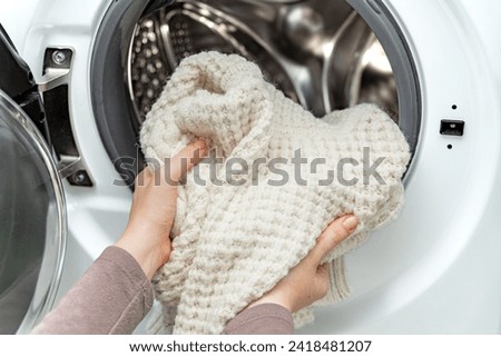 Woman putting white wool sweater into the drum of a washing machine in laundry room. Washing dirty clothes in the washer Royalty-Free Stock Photo #2418481207