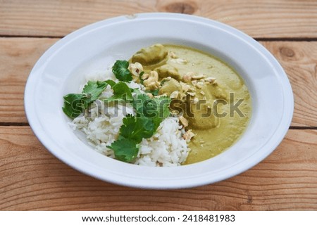 Close up picture of deep rustic porcelain plate with sweet and spicy indian style green lamb curry sprinkled with roasted cashew nuts and served with fresh coriander leaves on the white basmati rice.