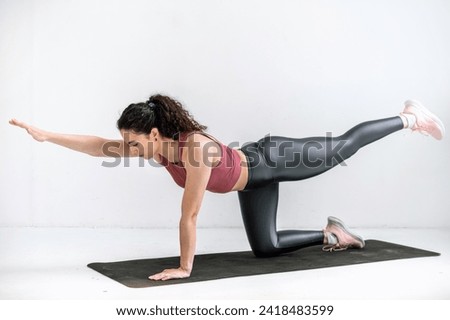Young woman in sport top and leggings practicing yoga, standing in bird pose on fitness mat in studio. Body balance, coordination exercises. Physical training at home Royalty-Free Stock Photo #2418483599
