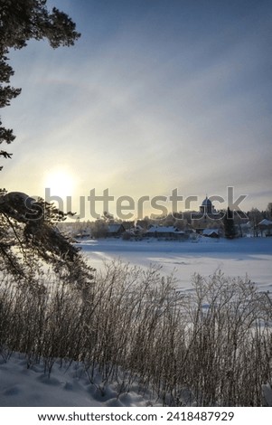 Winter landscape with pine, sun, frozen river and cathedral