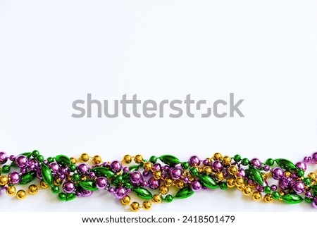 Mardi Gras background. Multicolored beads on white background. Fat Tuesday symbol. Festive decorations in gold, green and purple colors for traditional holiday. Copy space.