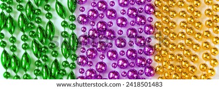 Mardi Gras background. Multi-colored beads close-up. Festive decorations in gold, green and purple colors for traditional holiday. Fat Tuesday symbol. Banner format.