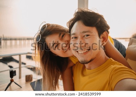 Happy Asian couple lover take selfie photo in the resort with romantic sunset at the sea. Royalty-Free Stock Photo #2418539599