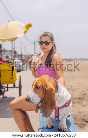 Latin woman drinking take away frappe sitting with a dog on the promenade next to a sandy beach