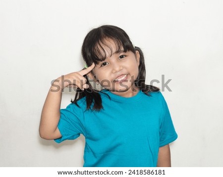 In blue attire, the girl smiles, her index finger on her forehead, portraying a thoughtful expression. Royalty-Free Stock Photo #2418586181