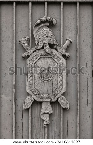 An ancient coat of arms in the form of a shield, two crossed swords and a helmet on an old gate.