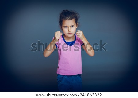 Girl child teenager brunette European appearance squeezed his hands into fists experiencing anger on a gray background cross process