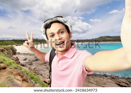 Happy Asian man taking selfie photo at the beach. backpaker, digital nomad and travelling concept. 