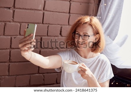 Freelance joy a red-haired woman takes a selfie during a coffee break.