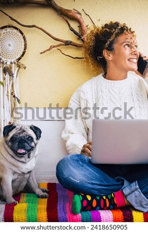 Funny work and technology concept picture with adult cheerful caucasian young beautiful woman calling at the phone and using laptop computer and cute lovely nice dog pug best friend near her