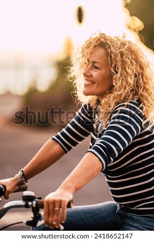 Cheerful beauiful blonde curly caucasian woman smile and enjoy the ride on a bike in outdoor leisure activity in the city - free and joyful active people on the street having fun Royalty-Free Stock Photo #2418652147