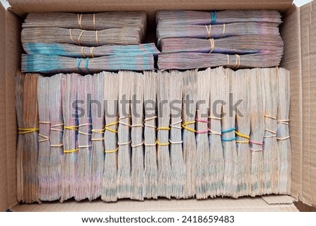 Cardboard box full of cash bundles.  Royalty-Free Stock Photo #2418659483