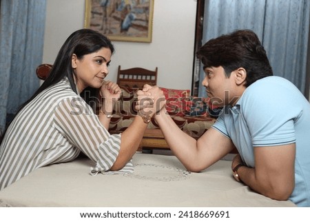 Indian young couple playing arm wrestle at home.
