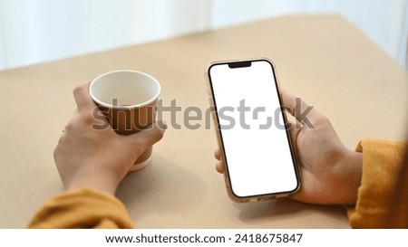 Closeup woman using mobile phone and drinking coffee at desk. Empty screen for application advertising