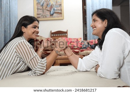Indian happy young daughter and mother playing arm wrestle in living room.